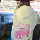 Person wearing a light green hoodie with a pink truck and palm tree design inside a vehicle.